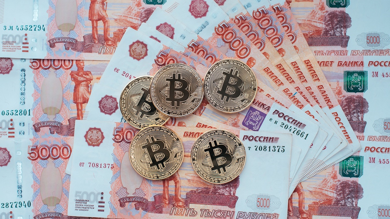 幾個旨在代表比特幣的金屬代幣放在桌子上的一堆俄羅斯 5000 萬盧布鈔票上。