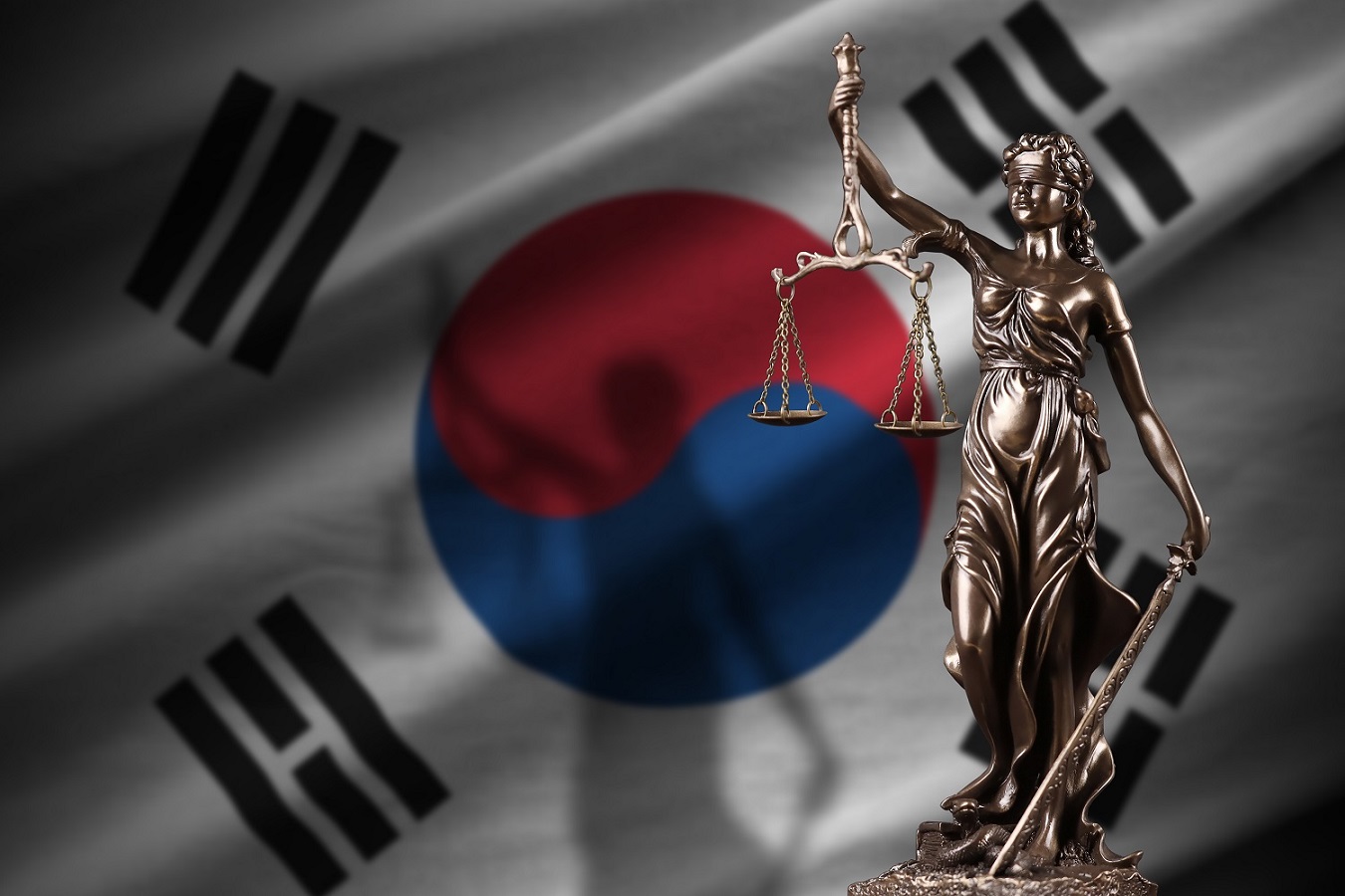 一尊正義女神的雕像，蒙著眼睛，拿著秤和一把劍，在韓國國旗前。
