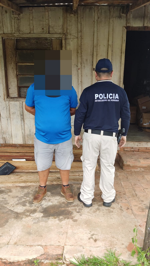 一名面部偽裝的男子站在巴拉圭執法人員旁邊戴著手銬。