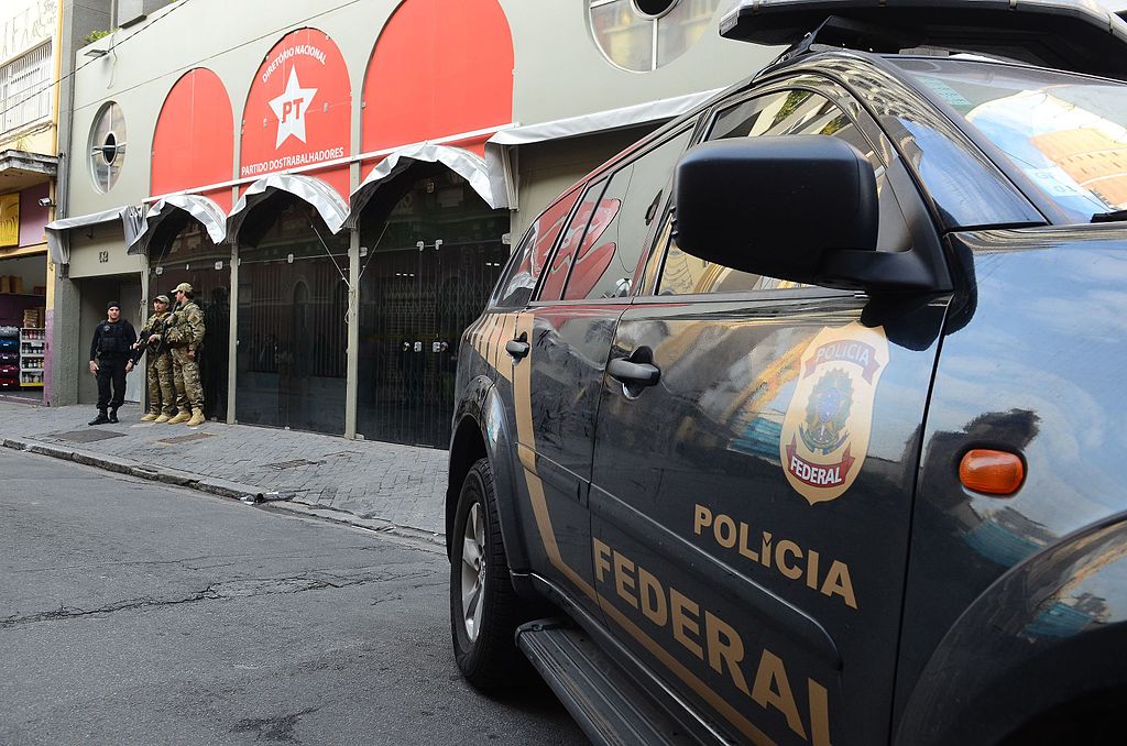 巴西武裝警察和軍官站在一棟建築物外，前景是一輛警車。